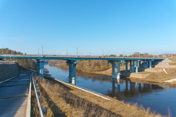 A new modern automobile bridge over the river on the background of the blue sky. A sturdy reinforced concrete bridge, thick concrete arches and metal floors.