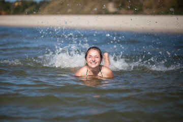 A woman splashes in the water, splashes flying in all directions. The woman smiles broadly and screams from the cold water