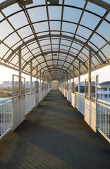 Vertical photo of a pedestrian bridge with railings and canopy in perspective in sunlight at sunset
