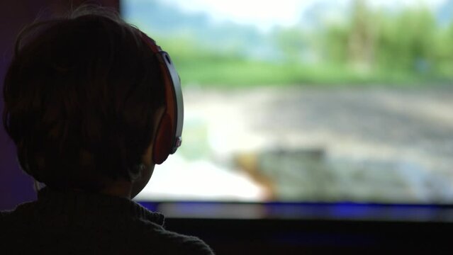 Child Gamer Playing Video Games on TV Screen. Boy in Headphones Playing Computer Video Game on Console at Night. Person in Headphones With Joystick Plays Video Game on Big TV screen. Online Games.