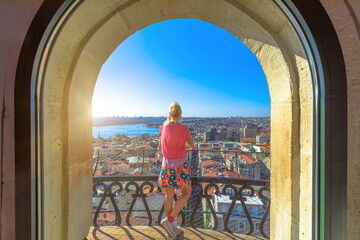  Back view of a woman enjoying a panoramic city view from an arched window of Galata Tower of Istanbul in Turkiye