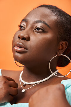 Portrait Of Pensive Plus Size African American Woman In Blue Long Sleeve Posing On Orange Backdrop