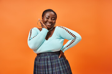 body positive african american woman in plaid skirt and blue long sleeve smiling on orange