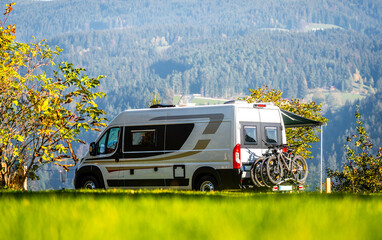 Campervan or motorhome with bicycle rack parked in the nature countryside. Camper van or  motor home is camping in a meadow surrounded by forest and hills. Active family vacation in Slovenia. © _jure
