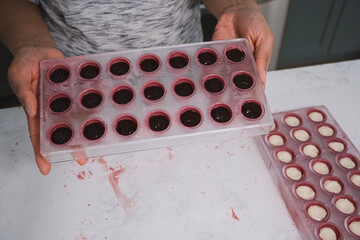 Kitchen work surface. Pink chocolate is poured into a plastic mold. Thickened chocolate spill. A woman holds in her hands a plastic mold filled with dark chocolate.