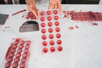 Kitchen work surface. Pink chocolate is poured into a plastic mold. Thickened chocolate spill. A woman holds in her hands a plastic mold filled with pink chocolate.