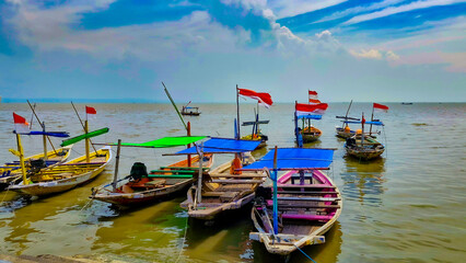 Obraz premium Several fishing boats made of wood and carrying red and white flags are moored at a small pier with a cloudy blue sky in the background
