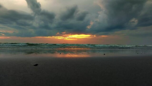 Cinematic ambient motion of the gentle soothing waves rolling in at the vast beach landscape with dramatic clouds