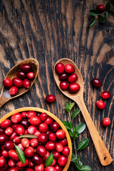 Fresh cranberries in a wooden bowl with spoon on dark wooden table. View from above.