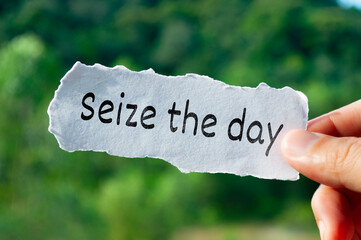 Seize the day text on torn paper with hand holding on nature background