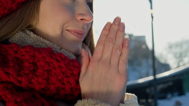 Close up face cute woman dressed knitted accessories trying warm her hands. Blowing arms with hot breath in frozen winter. Way to save herself in cold weather. Forest atmosphere