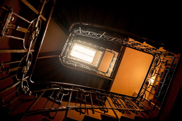 Looking up at the spiral staircase in old house. Dark staircase filled with warm interior light. 