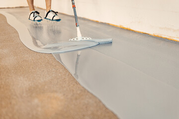 A construction worker apply grey epoxy resin in an industrial hall