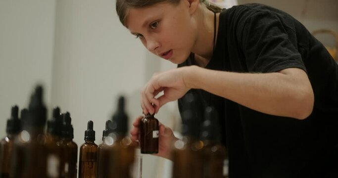 A teenage girl at a master class on making scented candles in the workshop chooses a scent for her candle. She studies the smells and chooses the appropriate one. DIY candle. Creative child.
