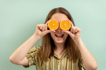 Portrait of a young woman holding orange slices over her eyes. Blue-green background.