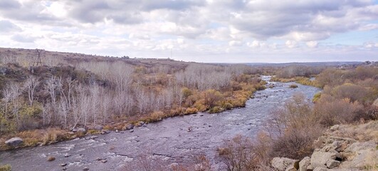 Rocky river bank among hills overgrown with vegetation, granite stones among dry yellowed grass