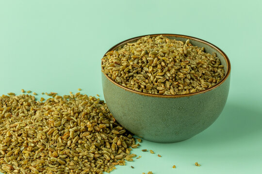 Uncooked freekeh in a bowl. A heap of grains on the table near the bowl. The cereal is made from immature, green, fire-roasted wheat.