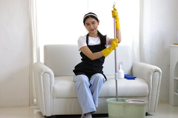 A young Asian woman who was tired from cleaning the house was relaxing on the sofa after mopping the floor.