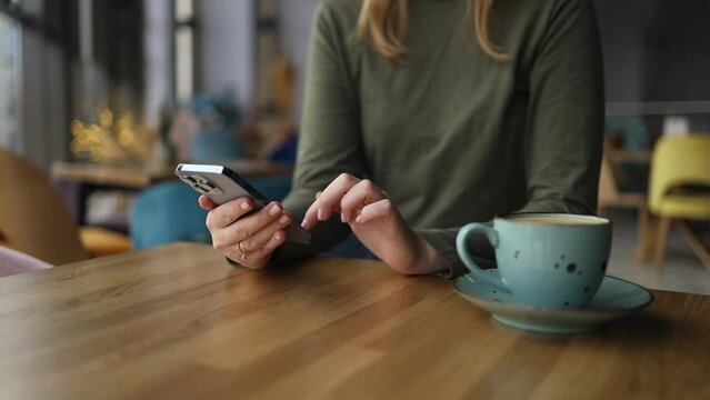 Close up of pretty female student used a cell phone. Woman hand holding texting using mobile on desk at coffee shop. Marketing business, technology. High quality FullHD footage