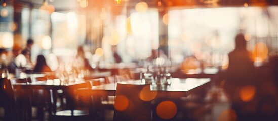 A blurred image of a restaurant interior, showcasing tables and chairs set up in the space. The background features a bokeh effect, adding a soft focus to the scene. - obrazy, fototapety, plakaty