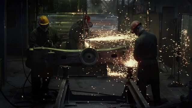 Workers are using grinders to work on a steel product at the metallurgy facility. Grinder tools are pushed against the product at metallurgy factory. Grinders smoothing the item at metallurgy factory.