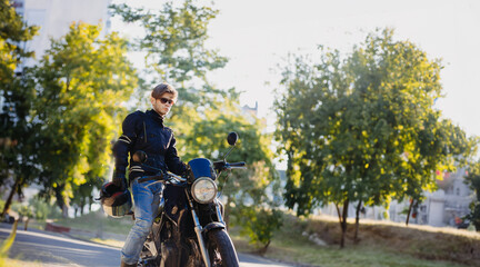 motorcyclist in outfit with motorcycle in sunglasses and jeans in summer