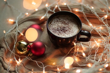 A cup with a hot Christmas drink among Christmas balls, garlands and lights. A burgundy cappuccino...