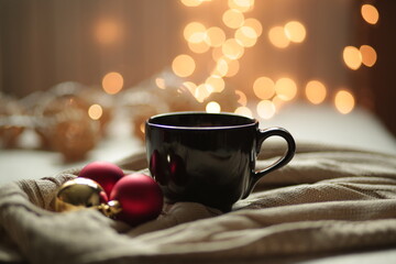 A cup with a hot Christmas drink among Christmas balls, garlands and lights. A burgundy cup on a...