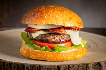homemade cheeseburger with fresh lettuce tomato onion crispy bacon juicy beef burger and melted cheese in a bun served on a natural wood log platter