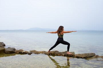 Woman practicing yoga by the sea on the rocks