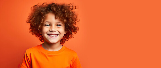 Cute handsome little boy with curly red hair and freckles wearing an orange T-shirt on an orange background. Place for text. Studio portrait of happy red-haired child - obrazy, fototapety, plakaty