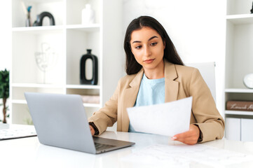 Work with documents. Focused serious indian or arabian business woman, financial manager, sit at workplace in the office with laptop, concentrated studying documents, create business plan and strategy