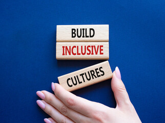 Build Inclusive Cultures symbol. Wooden blocks with words Build Inclusive Cultures. Beautiful deep blue background. Businessman hand. Business and Build Inclusive Cultures. Copy space.