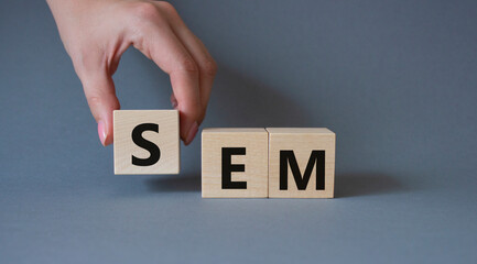 SEM - Search Engine Marketing symbol. Wooden cubes with words SEM. Businessman hand. Beautiful grey background. Business and SEM concept. Copy space.