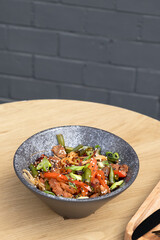 Bowl of udon noodles, veal and fried vegetables angle view on wooden table