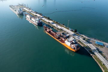 Aerial view of an industrial port with cargo and fuel tanker ships docked for loading and unloading.