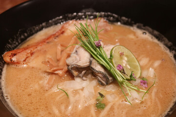close up of oyster ramen with lemon, noodle and spring onion in a black bowl