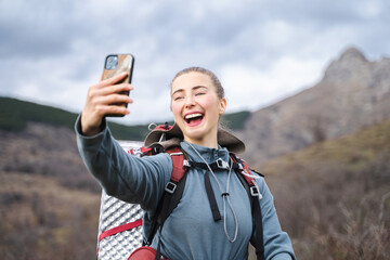 Smiling backpacker woman taking selfie with smart phone, happy backpacker greeting someone vie...