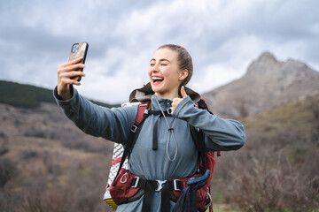 Smiling laughing hiker woman with backpack showing thumb up gesture while making selfie, camper...