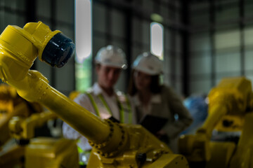 Factory engineers inspecting on machine with smart tablet. Worker works at heavy machine robot arm. The welding machine with a remote system in an industrial factory. Artificial intelligence concept.