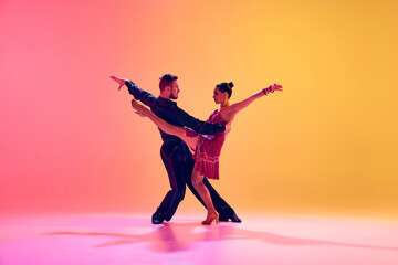 Elegant young woman and handsome man, ballroom dancers in motion, dancing against gradient pink yellow background in neon light. Concept of dance class, hobby, art, dance school, talent