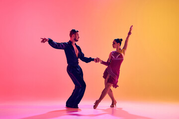 Male and female dancers performing a Latin dance in stylish clothes against gradient pink yellow background in neon light. Concept of dance class, hobby, art, dance school, talent