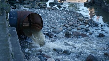 Corroded industrial pipe leaking polluted water into river, reflecting environmental degradation. 