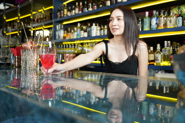 Asian woman bartender in uniform shaking Stanley cups, mixing cocktails, serving drinks at a party...