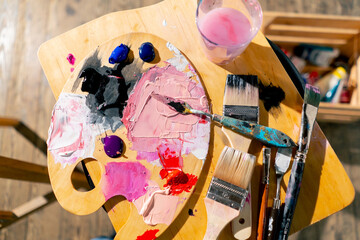 close-up top shot in an art workshop there is a palette on stool palette knife a glass of solvent