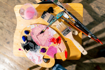 close-up top shot in an art workshop there is a palette on stool palette knife a glass of solvent