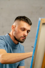 young artist in a blue t-shirt in an art studio working on painting while sitting