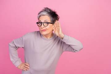 Photo of funny expression mature age woman touch ear listening copyspace hearsay secrets isolated over pastel pink color background