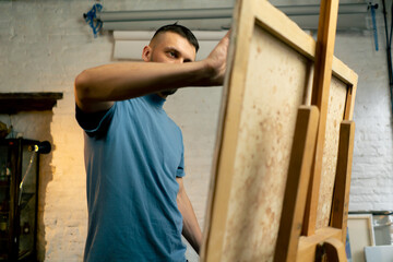 in an art workshop an artist in a blue T-shirt makes broad strokes on the canvas with wide and flat...
