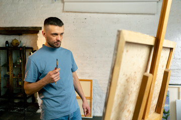 in an art workshop an artist in a blue T-shirt is thinking about where to make a stroke with palette knife
